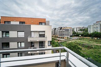 Balkonový výhled na moderní bytové domy s velkými okny a šedou fasádou, nacházející se v klidné městské čtvrti.