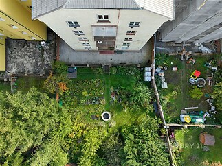 Zahrada u bytového domu s travnatým porostem, zahradními záhony a kompostérem. Klidné prostředí vhodné pro relaxaci a pěstování rostlin.