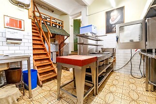 Industriální kuchyň s dlažbou, nerezovými pracovními stoly a schody. Funkční prostor s vestavěným úložným systémem a světlým osvětlením.