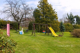 Zahrada s dětským hřištěm, skluzavkou a houpačkami, obklopená stromy a keři, ideální pro rodinný odpočinek na čerstvém vzduchu