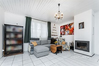 Světlý obývací pokoj s dlažbou a krbovými kamny, moderní dekorace s velkými okny, pohodlná šedá pohovka a designové osvětlení.