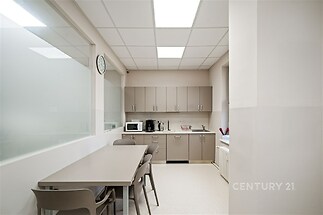 Moderní kuchyň s vestavěnými skříněmi a světlou dlažbou, nabízí prostorný jídelní kout a minimalistický design vhodný pro kancelářské prostředí.