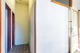 Prázdná chodba s bílými stěnami, kobercovým povrchem a dřevěnými dveřmi, ideální pro renovaci a přizpůsobení osobnímu stylu.