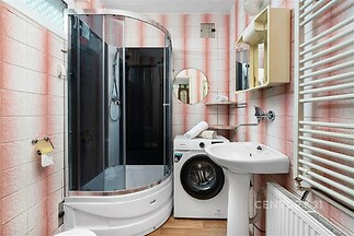 Kompaktní koupelna s parketovou podlahou, sprchovým koutem a pračkou. Světlé dlaždičky dodávají místnosti čistý a moderní vzhled.