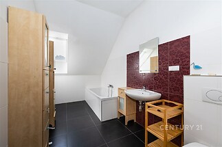 Světlá koupelna s dlažbou, prostornou vanou a dřevěným nábytkem, moderní design a přirozené světlo díky střešnímu oknu