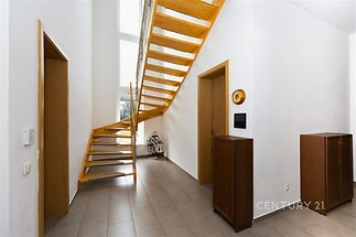 Prostorná chodba s dlažbou a dřevěným schodištěm, moderní interiér, velká okna poskytují přirozené světlo