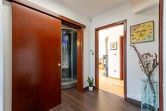 Chodba s dřevěnou podlahou, moderní design, sprchový kout s masážními tryskami, dekorativní rostlina v rohu, světlý interiér.