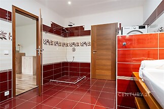 Prostorná koupelna s červenou dlažbou, moderní sprchou a dřevěnými dveřmi, vybavená pračkou a keramickými obklady s květinovým vzorem.