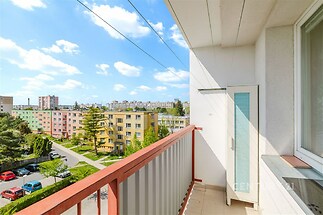 Balkon s výhledem na sídliště, moderní dlažba, prostorné zábradlí, světlé okolí, výšková budova, městská zástavba, výhled do zeleně