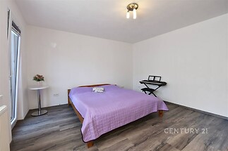 Prostorná ložnice s moderní parketovou podlahou, velkými okny a světlým interiérem nabízí klidné prostředí pro odpočinek.