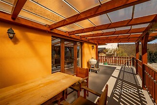 Krytá terasa s dřevěným nábytkem, proskleným stropem a dlažbou nabízí příjemný venkovní prostor.