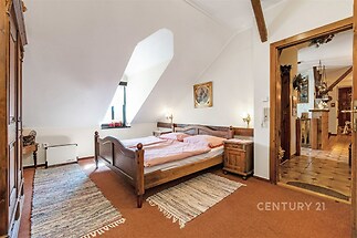 Prostorná ložnice s dřevěným nábytkem, parketovou podlahou a velkými okny nabízí útulnou atmosféru a tradiční styl.