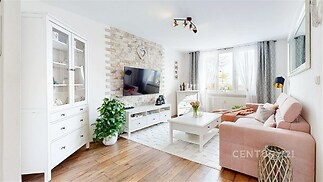 Světlý obývací pokoj s parketovou podlahou, velká okna a moderní interiér. Zděná stěna s krbem dodává útulný a elegantní styl.