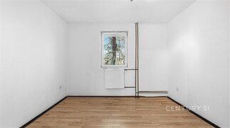 Prázdný pokoj s parketovou podlahou, bílými stěnami a oknem s výhledem na přírodu, vhodný pro rekonstrukci a vlastní designové úpravy.