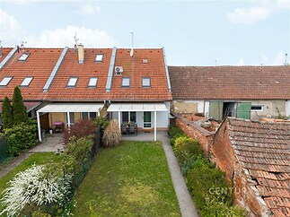 Řadový rodinný dům s červenou střešní krytinou, zastřešenou terasou a zelenou zahradou, zasazený v řadě podobných budov.