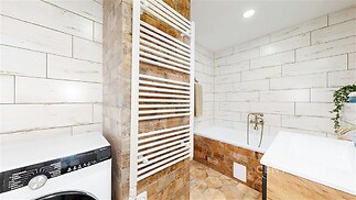 Moderní koupelna s béžovou dlažbou, vanou a topným žebříkem, světlá stěna z imitace dřeva, kvalitní spotřebič, útulný vzhled.