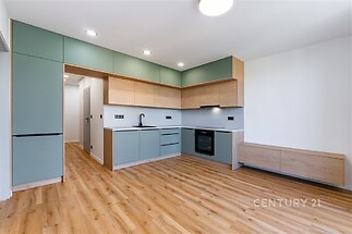 Moderní kuchyň s parketovou podlahou, matné zelené skříňky, dřevěné detaily, vestavěné spotřebiče, světlý a čistý design.