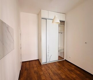 Prostorná ložnice s parketovou podlahou, vestavěnými skříněmi a moderními bílými stěnami, ideální pro pohodlné bydlení.