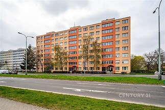 Vícepodlažní bytový dům s oranžovou a béžovou fasádou, upravené okolí, parkovací místa, blízkost městské infrastruktury, moderní výstavba.