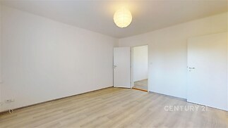 Prázdný pokoj s moderní parketovou podlahou, bílými stěnami a jednoduchým osvětlením, ideální pro přizpůsobení osobním potřebám.