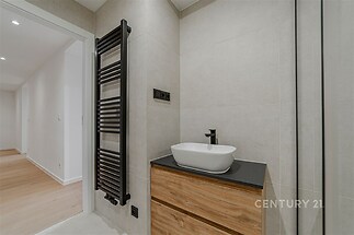 Koupelna s moderním umyvadlem, dřevěnou skříňkou a černým topným žebříkem, stylové dlažby, elegantní provedení.