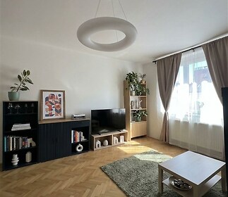 Světlý obývací pokoj s parketovou podlahou.