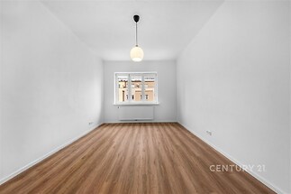 Světlý obývací pokoj s parketovou podlahou a velkými okny, moderní a světlý interiér ideální pro bydlení v centru města.