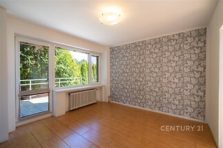 Světly obývací pokoj s parketovou podlahou a velkými okny, moderní tapeta na stěně, přístup na balkon.