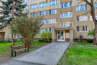 Vstup do bytového domu s udržovanou zahradou, světlá fasáda a plastová okna, moderní prostředí, lokalita plná zeleně.