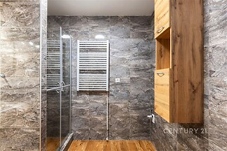 Koupelna s moderním designem, obklady s mramorovým vzorem, prosklený sprchový kout a dřevěná skříňka poskytují elegantní vzhled