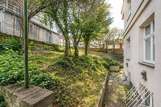 Zahrada s travnatým porostem, vzrostlými stromy a terénní úpravou vedle rekonstruované budovy, ideální pro relaxaci a soukromí.