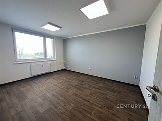 Světlý obývací pokoj s plastovými okny, parketovou podlahou a moderním minimalistickým stylem, vytváří příjemný prostor pro bydlení.