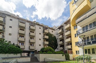 Moderní bytový dům s balkony, světlá fasáda, upravená zeleň, klidná lokalita, atraktivní městské bydlení.