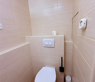 Moderní koupelna s hladkými dlaždicemi, světlé béžové dlažby a vestavěná toaleta, minimalistický styl a čisté linie.