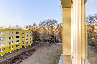 Výhled z okna na světlý exteriér, žlutá fasáda budovy, zelená plochy, klidná lokalita, perfektní pro rodinné bydlení.