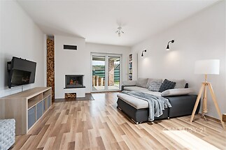 Světlý obývací pokoj s parketovou podlahou, moderní krbová kamna a velká okna, které zajišťují dostatek přirozeného světla