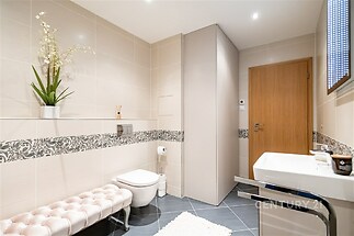 Světlá koupelna s moderní dlažbou, elegantní obklady a dřevěné dveře, doplněná stylovým dekorem a vestavěným úložným prostorem.