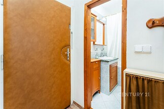 Malá koupelna s dlažbou a dřevěným nábytkem nabízí praktické úložné prostory, světlý interiér podtrhuje zrcadlo nad umyvadlem.