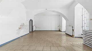 Prázdný pokoj s dlažbou, vyklenutými stropy a bílými stěnami. Prostor má velká okna a působí světlým dojmem, ideální pro moderní úpravy.