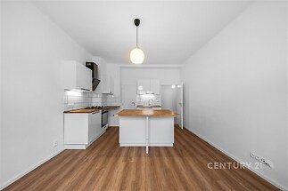 Moderní kuchyň s dřevěnou podlahou, bílými skříněmi a ostrůvkem, nabízí vestavěné spotřebiče a elegantní osvětlení, ideální pro rodinnou domácnost.