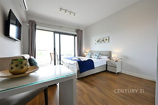 Světlá ložnice s parketovou podlahou, velkými okny a moderním dekorem, nabízí útulné a stylové prostředí vhodné pro relaxaci.
