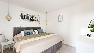 Prostorná ložnice s moderní dekorací, laminátová podlaha, závěsné osvětlení, světlé stěny, elegantní atmosféra.