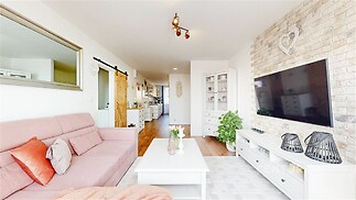 Světlý obývací pokoj, moderní styl, parketová podlaha, dominantní kamenná stěna, velké okno zajišťující přirozené světlo, útulná atmosféra.