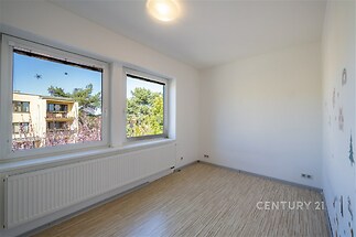 Světlý dětský pokoj s parketovou podlahou, velkými okny a výhledem do zeleně, v moderním udržovaném bytě.