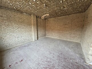 Prázdná místnost s odhalenými cihlovými zdmi a dřevěným stropem, vyžadující rekonstrukci, s betonovou podlahou připravenou pro úpravy.