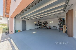 Prostorná garáž s betonovou podlahou, dílenským koutkem a vestavěnými policemi, ideální pro moderní uspořádání a úložný prostor.