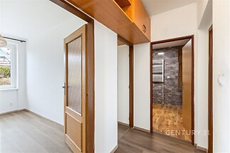 Předsíň s parketovou podlahou, dřevěnými dveřmi a vestavěnými skříněmi nabízí přístup do moderní koupelny s dlažbou.