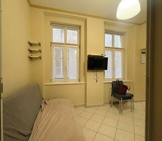 Malý obývací pokoj s dlažbou, dvěma velkými okny a béžovými stěnami, udržovaný ve světlém stylu.