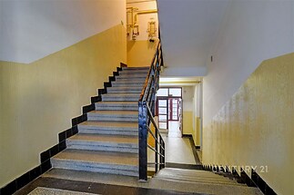 Schodiště s dlažbou, kovovým zábradlím a světlými stěnami, vedoucí do bytu v rekonstruované budově.