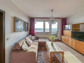 Světlý obývací pokoj s kobercem, velká okna s balkonem, klasická sedací souprava, dřevěná obývací stěna, vše v retro stylu, původní stav.